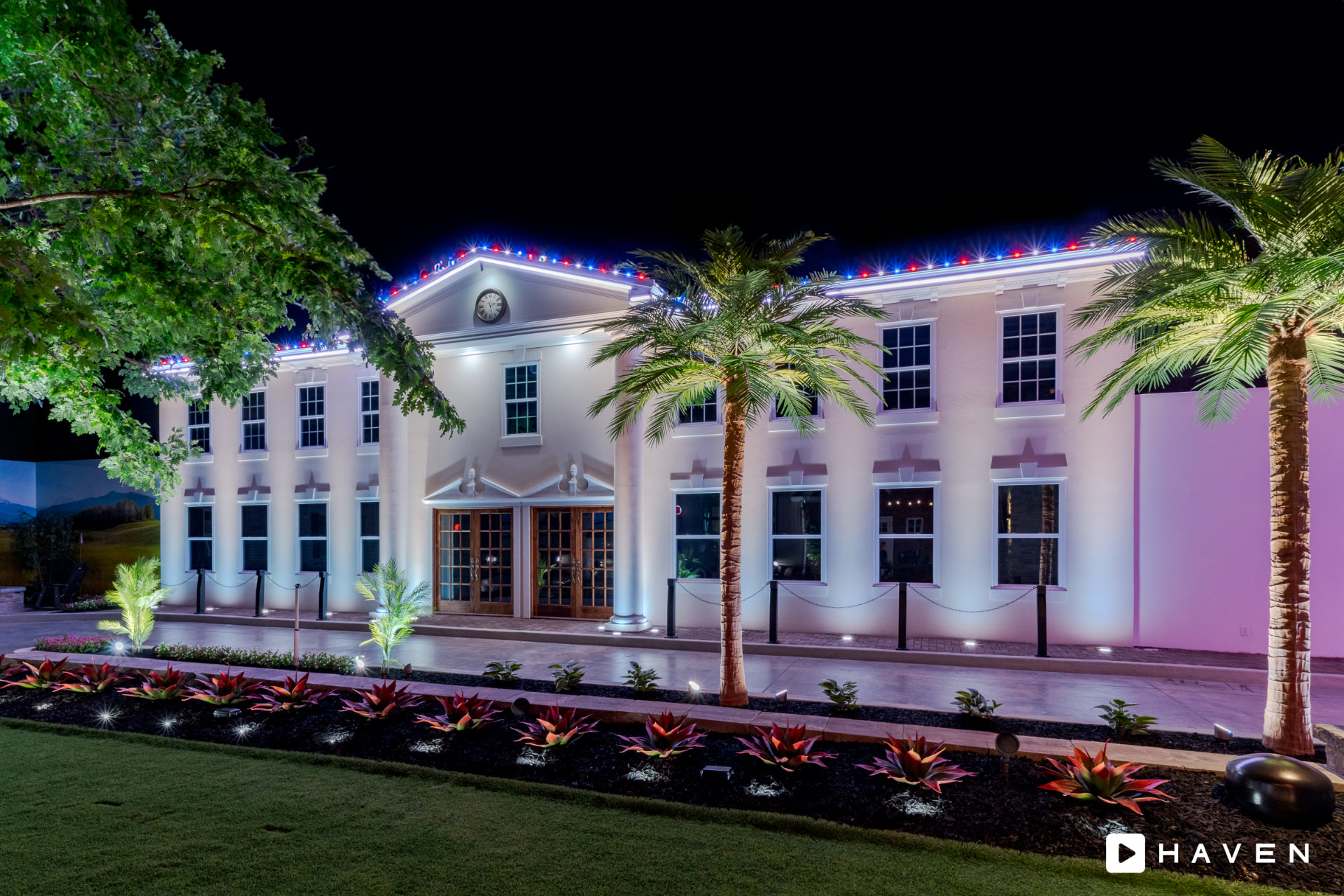 Building facade in red, white and blue roofline lighting with landscape uplighting