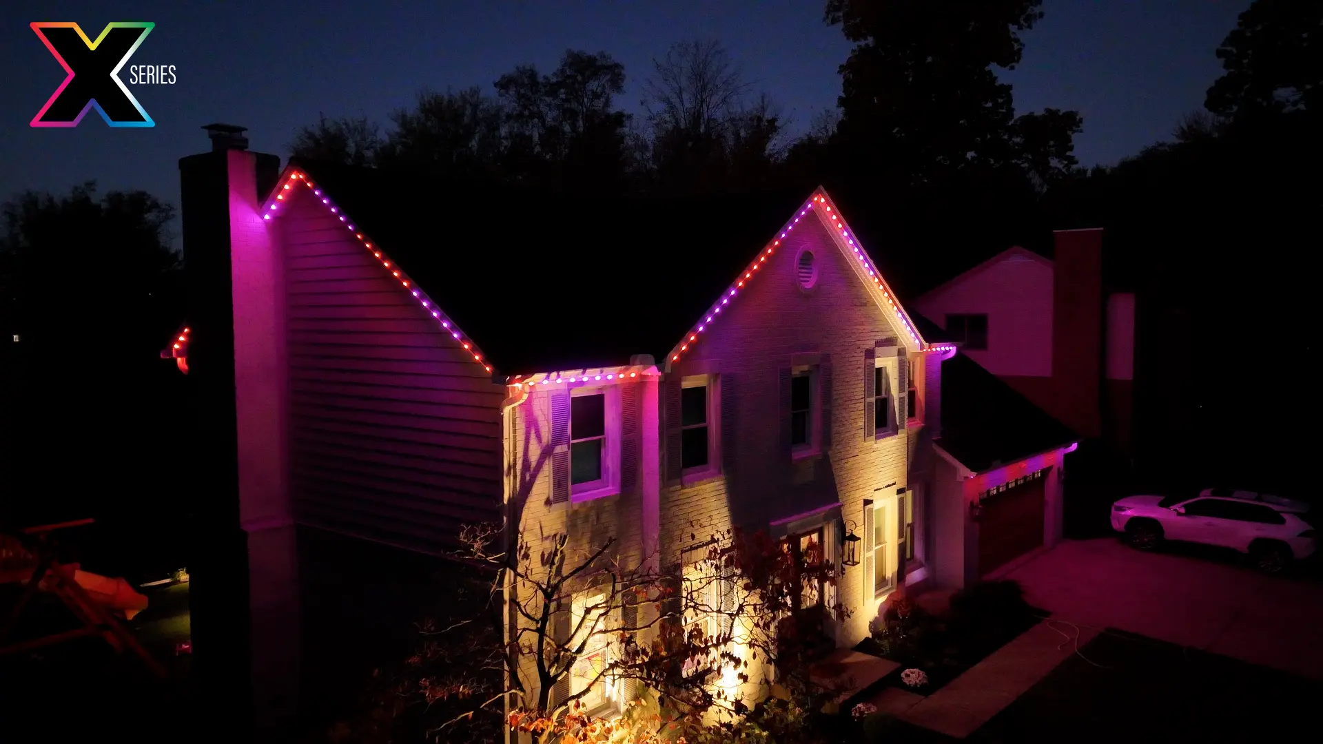 Two-story home lit in pink and purple permanent roofline lighting at night