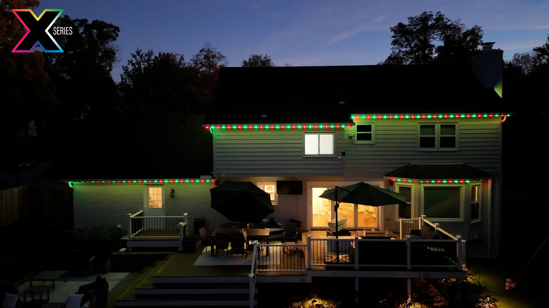 Rear of a home in red and green holiday roofline lighting above a deck
